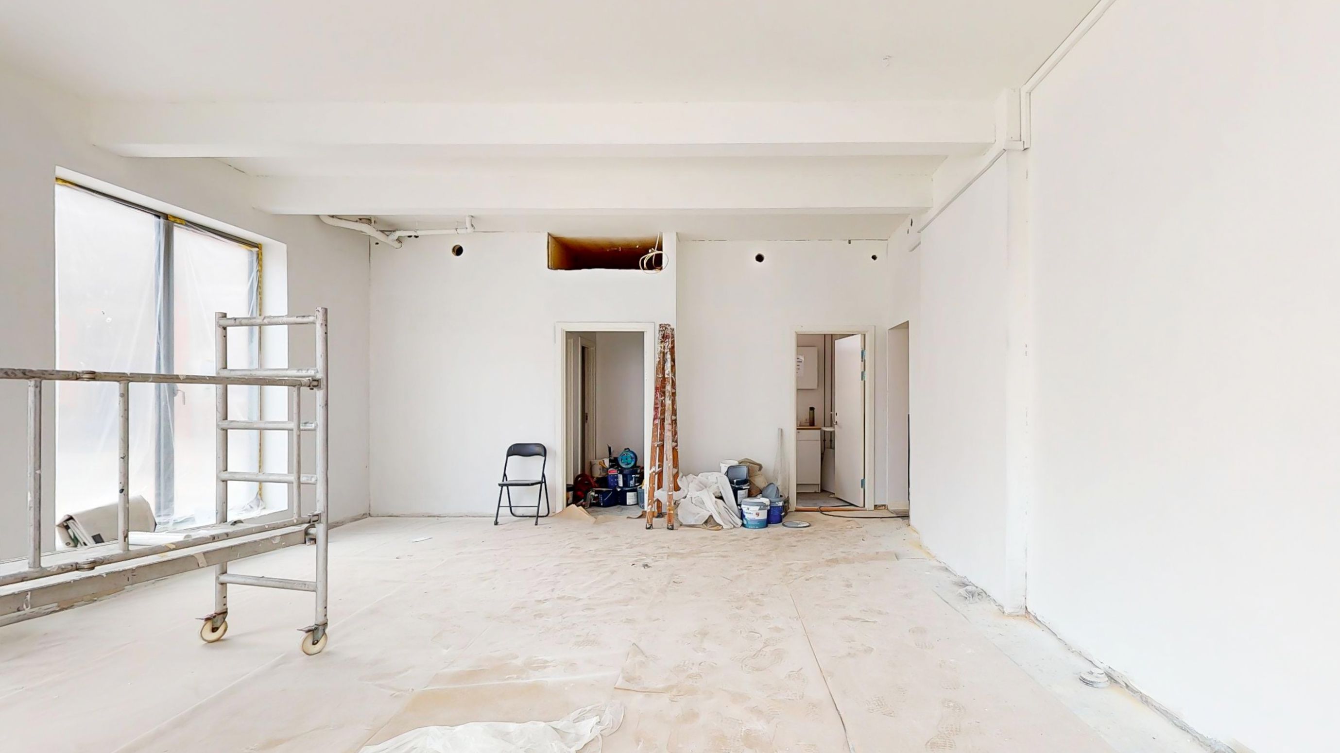 Renovering af butikslokal med renset væg, stol og skrald, bjælkeloft og åbne døre, værktøj og materialer og vinduesglas