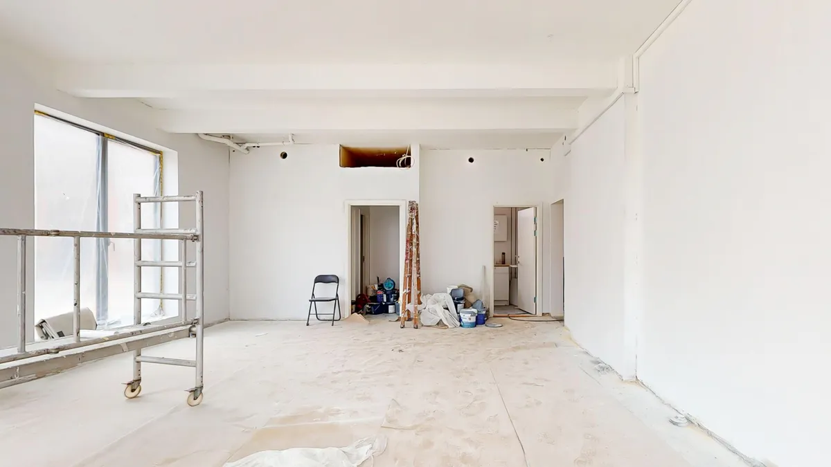 Renovering af butikslokal med renset væg, stol og skrald, bjælkeloft og åbne døre, værktøj og materialer og vinduesglas