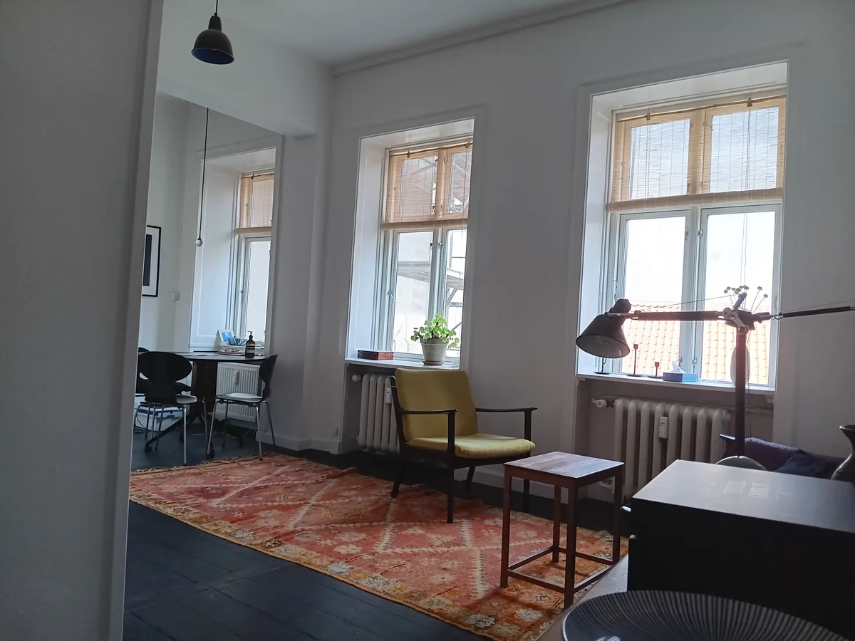 Foto af indretning med møbler og vinduer i en lyse stue, hvor der er en lysegul stol og en gul gulvmåtte