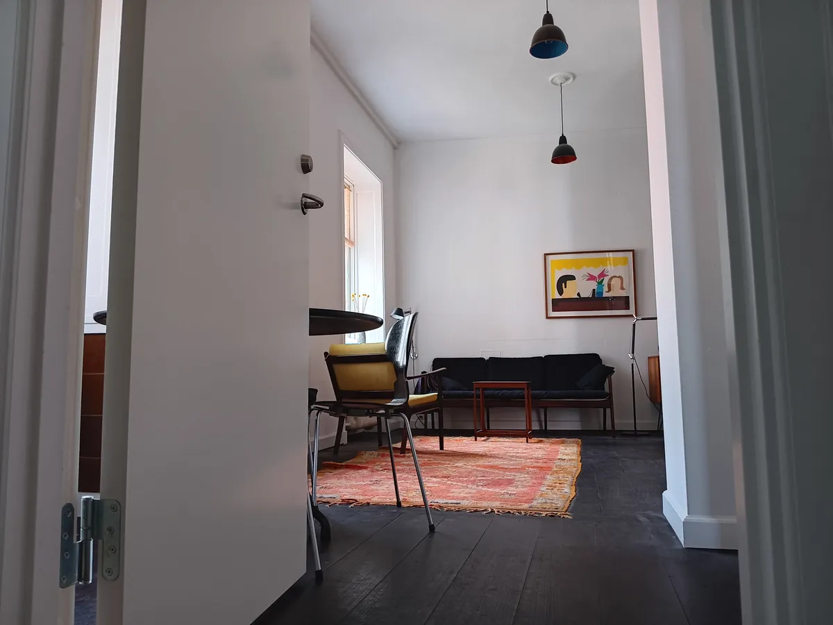 Lyst og elegant værelse med turkisgule stole og mørkt trægulv. Loftslejlighed med lyse loftshøjder og moderne møbler. På væggen hænger en farverig maleri.