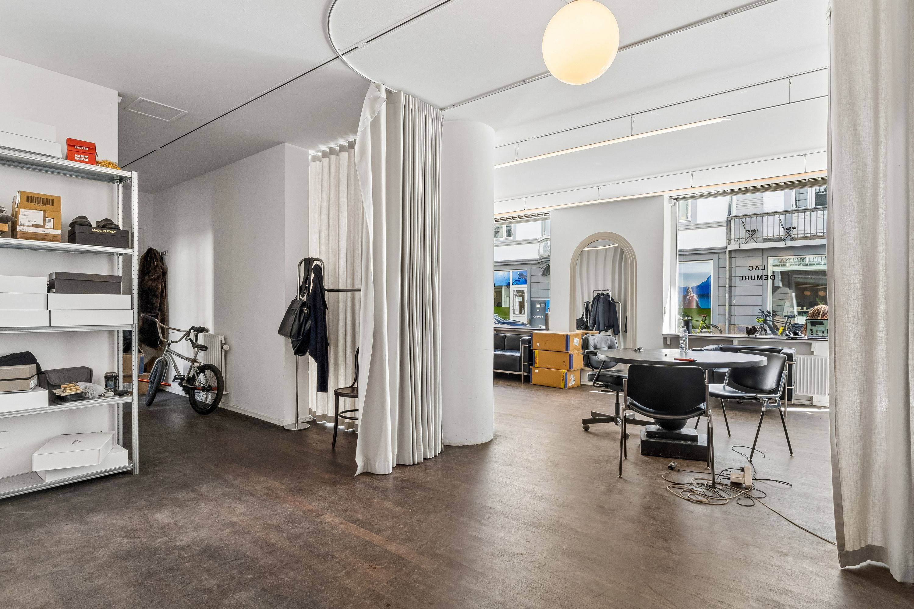 Et værelse med hvide vægge og loft, en stor hvid søjle og hvide gardiner, to stole og et bord, og et højreguleringssystem på gulvet.