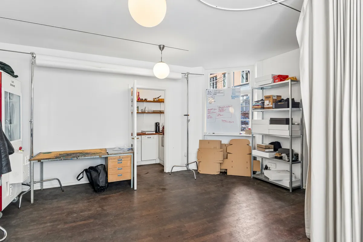 Lejlighed til leje med stort rum, bord, skrivebord, køleskab og stålampe samt lynlåsdør og glasvinduer til lyset