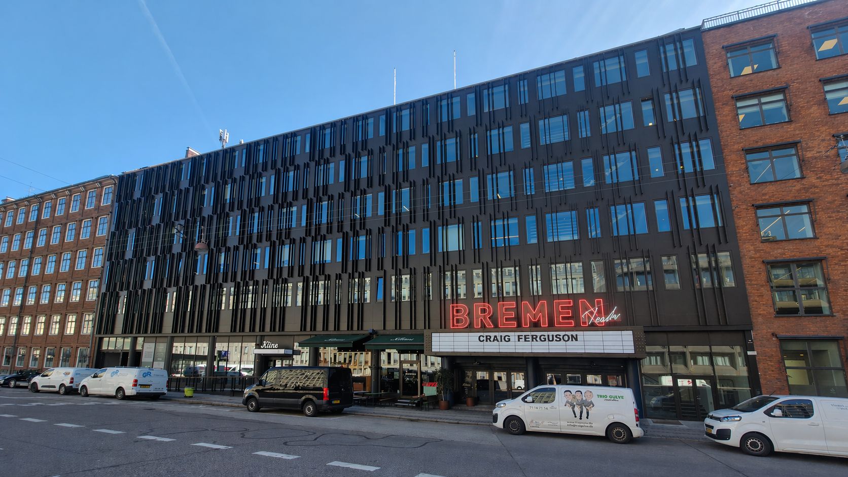 Kontorbygning med flere indretningsmuligheder og størrelser. Bremen Teater med rødt neon lys. Parkerede hvide og sorte biler på gade. Søjle og rødt neon lys i forgrunden.