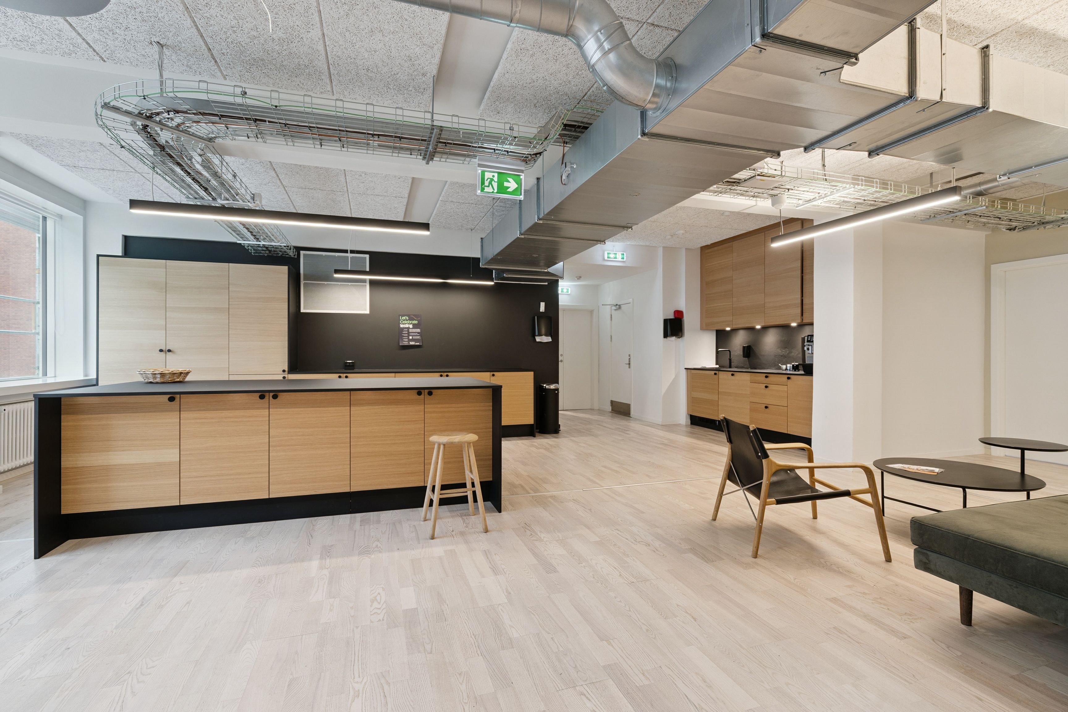 Kontorområde med åbent køkken, massivt bord og stole, lys, trægulve, moderne indretning, højt loft og lysepunkter