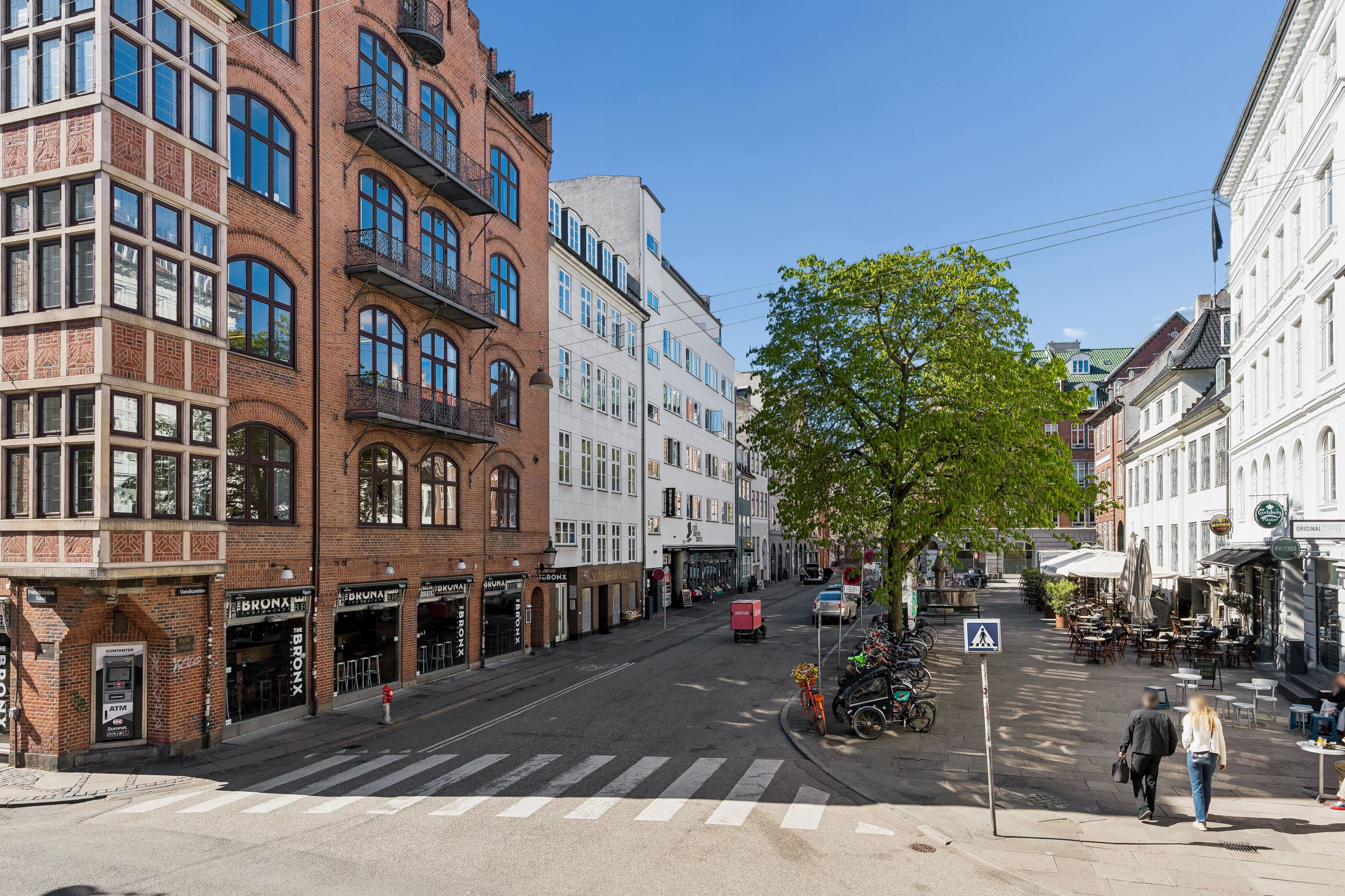 Kontor på Vandkunsten i København K. Mennesker går på fortov med cafébord, træer og huse med mange vinduer og balkoner