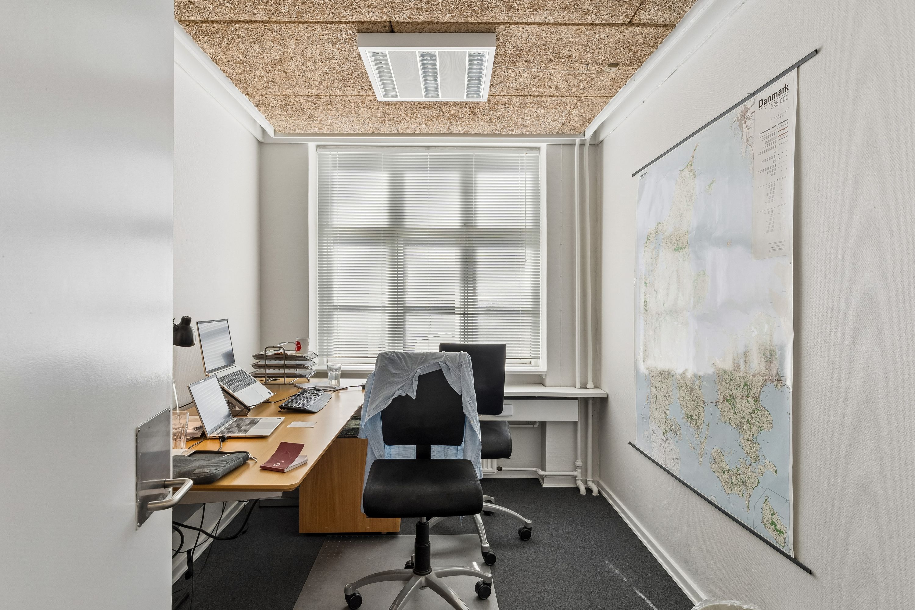 Kontor med lysevinduer, moderne skrivebord og to ergonomiske kontorstole samt en større kortudstilling af Danmark på væggen