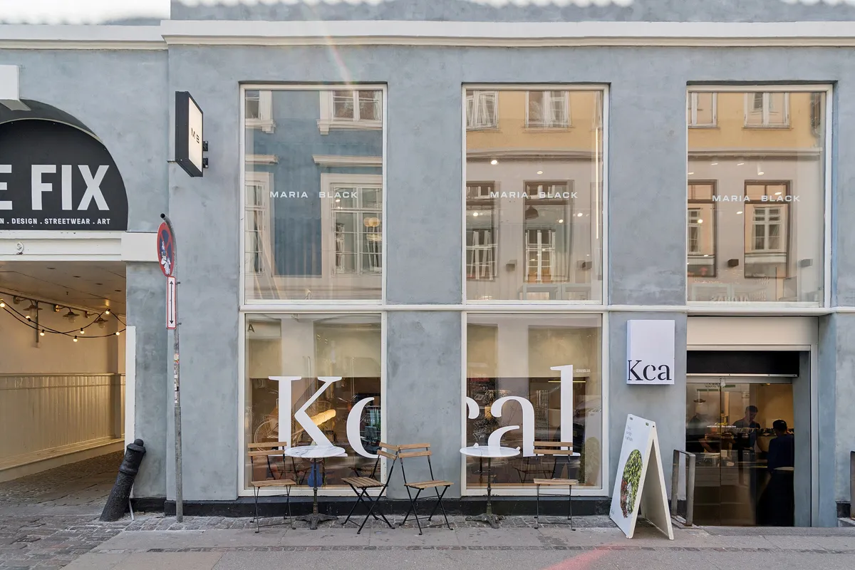 En butiksfront med store glasruder og store lyse skrifttyper med Kcal og Maria Black på ruderne