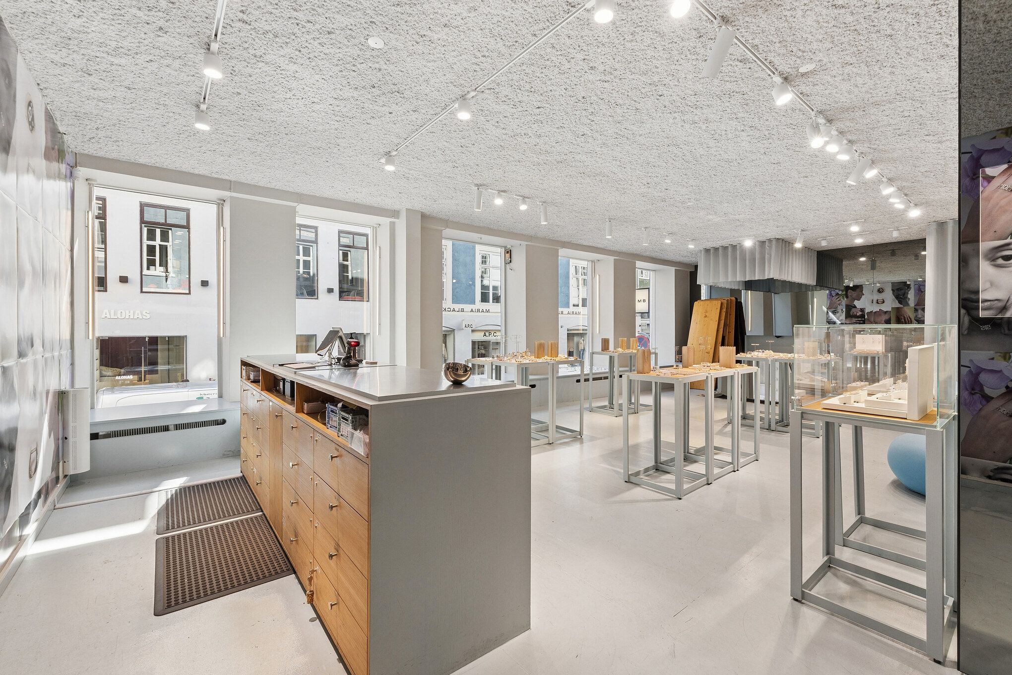 Et stilfuldt butikslokale med minimalistisk design, store vinduer, møbler og lysekroner, forskellige udstillinger og rekvisitter, og en luksuriøs atmosfære, der tiltrækker kunder og opfordrer til shopping
