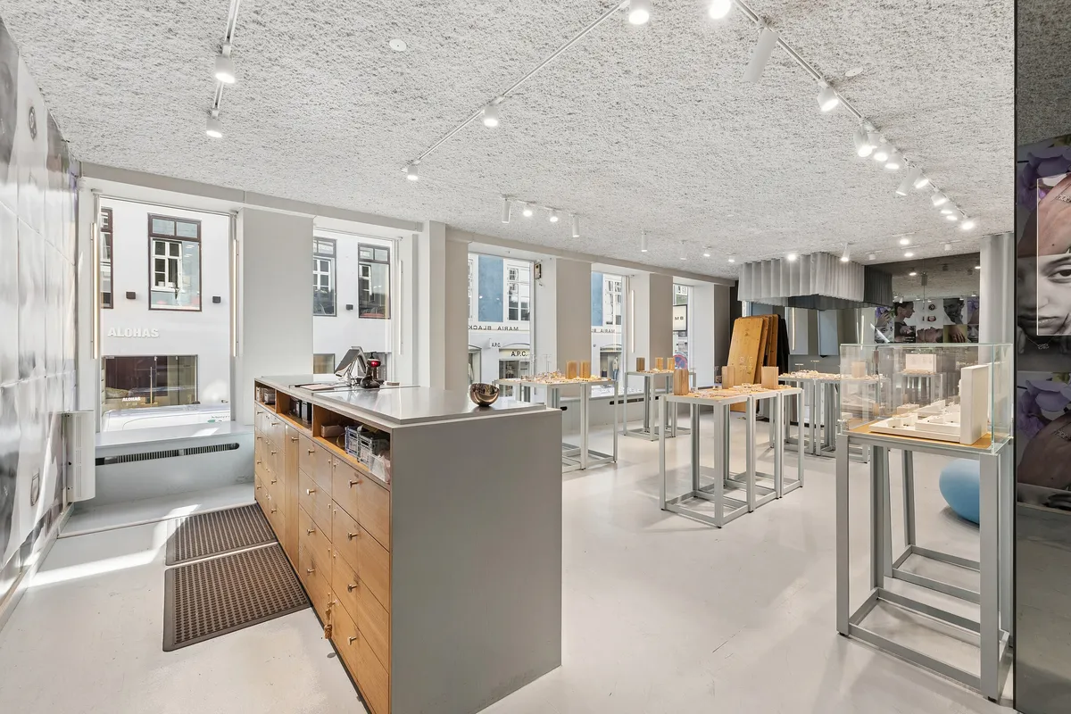 Et stilfuldt butikslokale med minimalistisk design, store vinduer, møbler og lysekroner, forskellige udstillinger og rekvisitter, og en luksuriøs atmosfære, der tiltrækker kunder og opfordrer til shopping