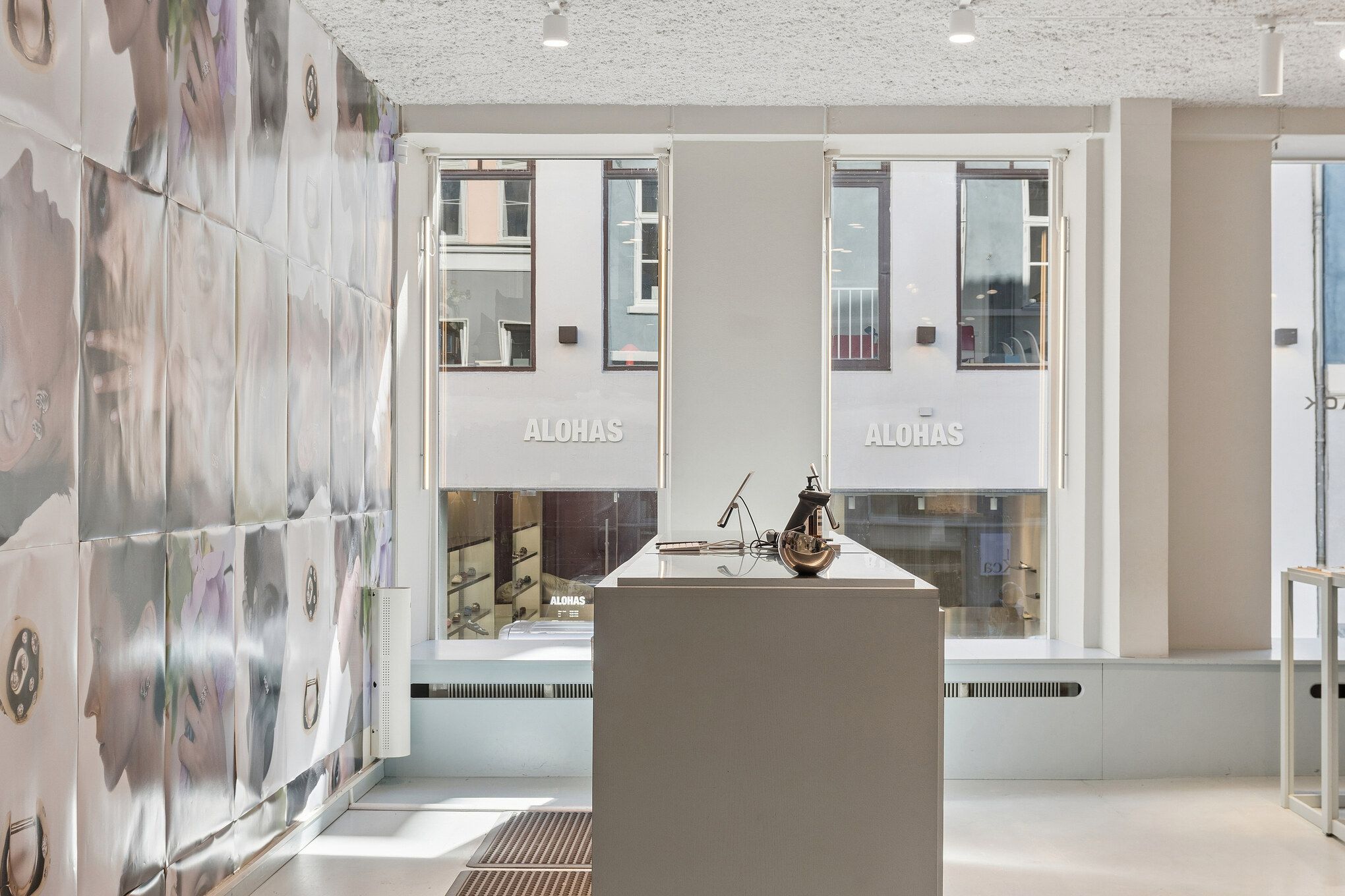 Minimalistisk design med stort loft, hvide vægge, moderne møbler og lyse vinduer med solbeskyttelse. Søjler med store skilte med teksten Alohas.