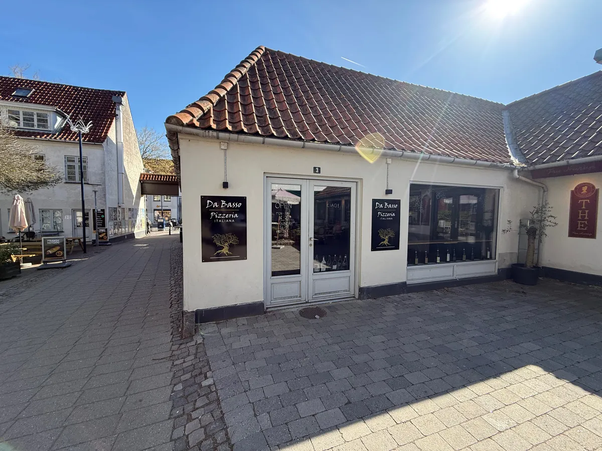 Take-away til leje i Kongens Lyngby. Opført i hvid mursten med to store vinduer og døre. Stående plante og to paraplyer. Nummer 3 på væggen.
