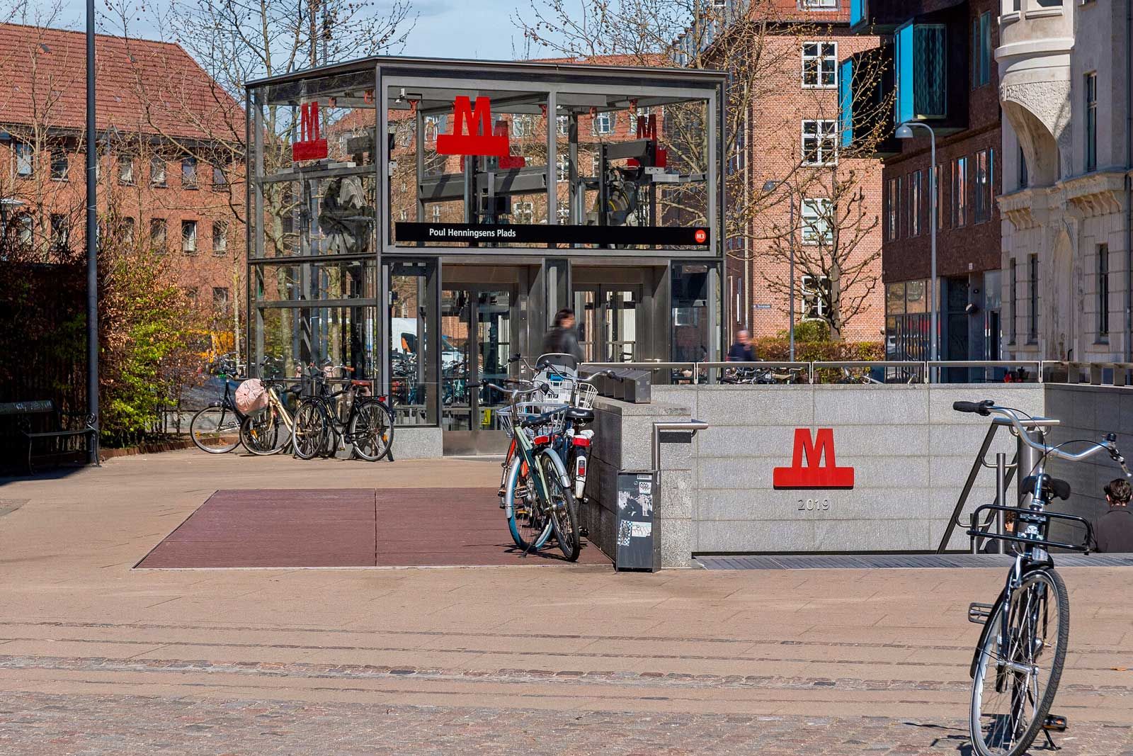 En moderne kontorplads med glasdækket indgang, tomme cykler parkeret og en gård med store røde bogstaver