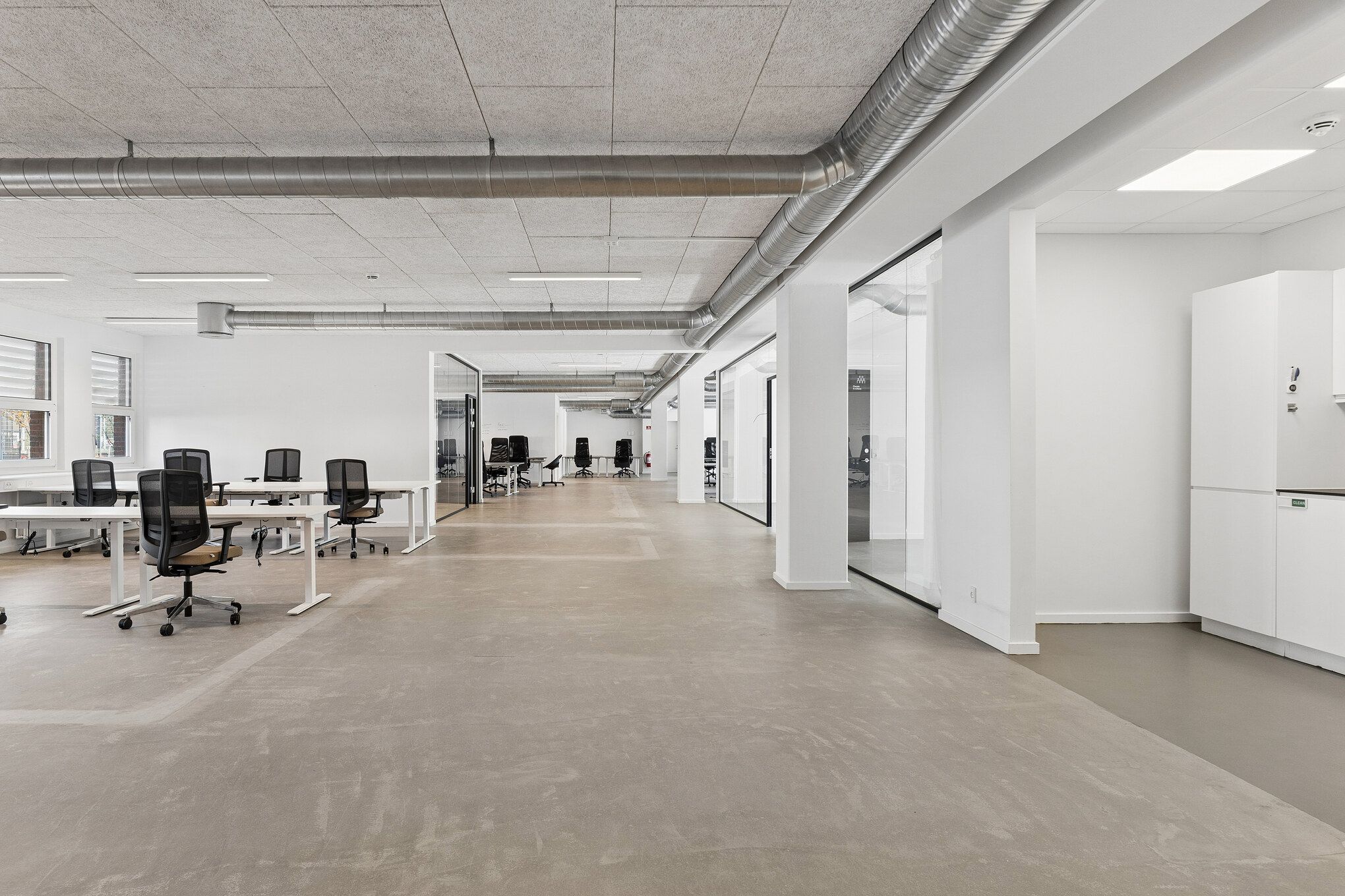 Moderne kontor med højt til loftet, hvide vægge og lyse lofter samt lysegulve og vinduer med gardiner