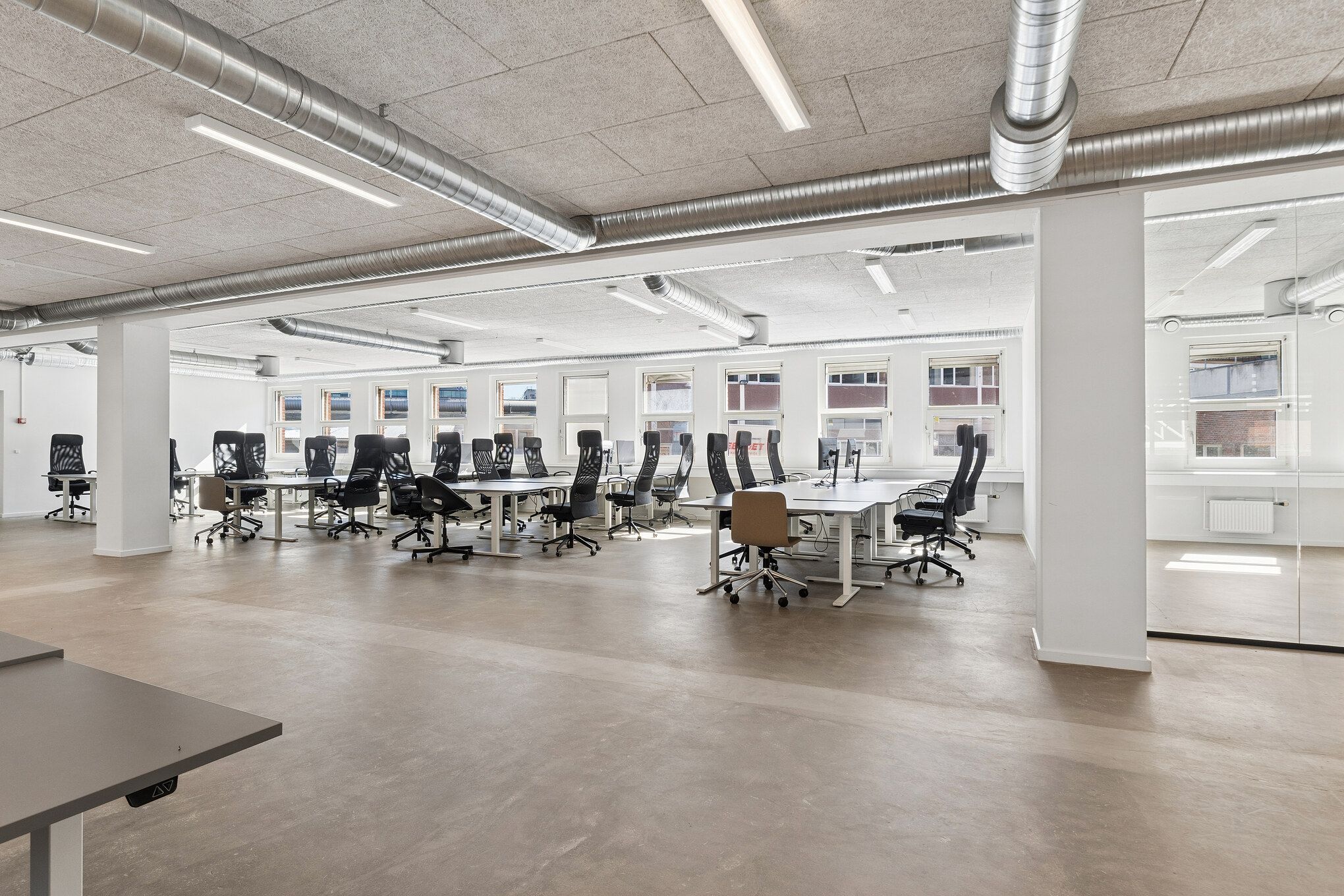 Kontor med store vinduer og moderne møbler, lyse lofter, lysegulv og slanke søjler