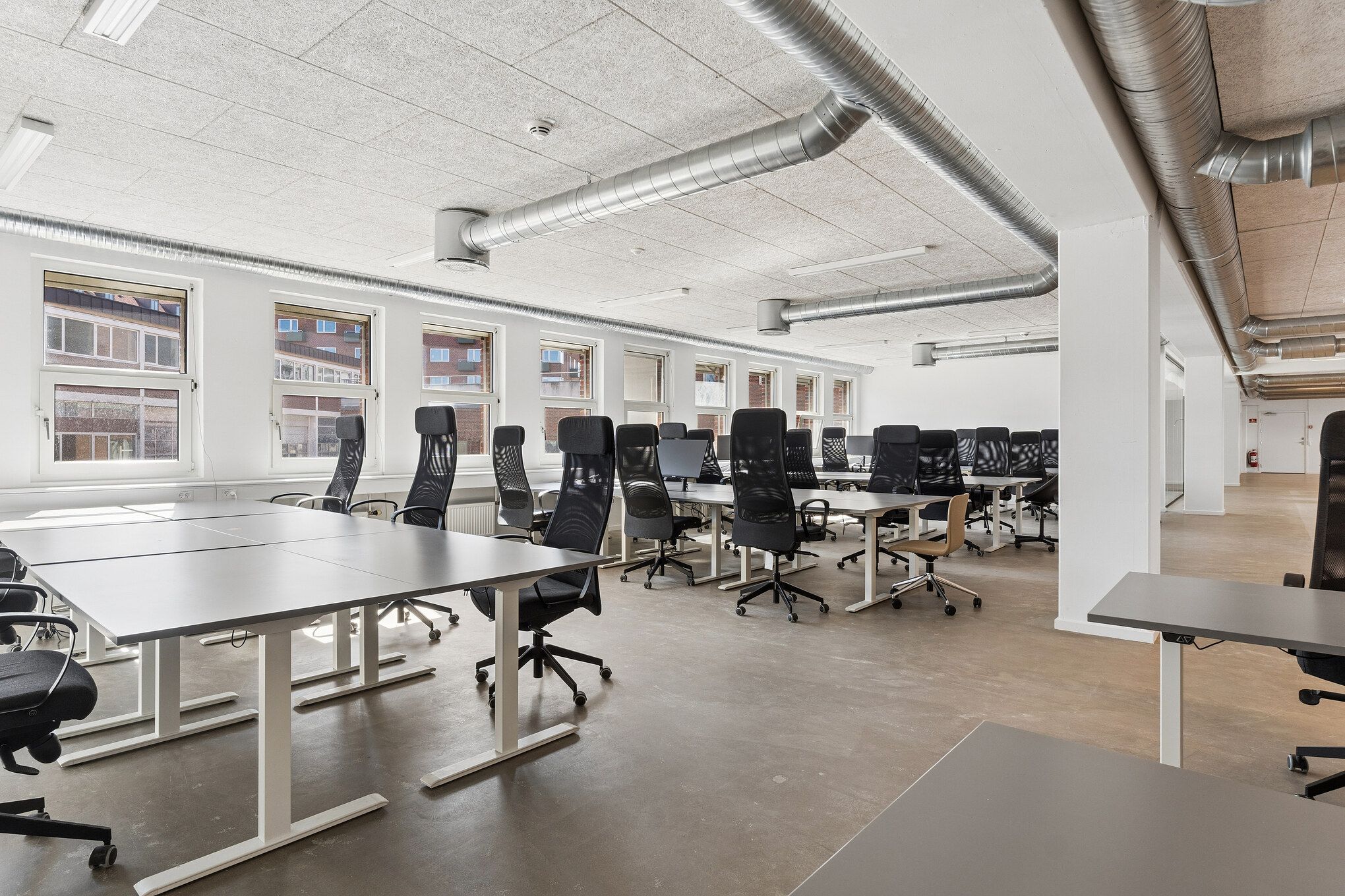 Kontorlokaler med højt til loftet og store vinduer med udsigt til byens grønne områder. Moderne hvide kontormøbler og teknologi.