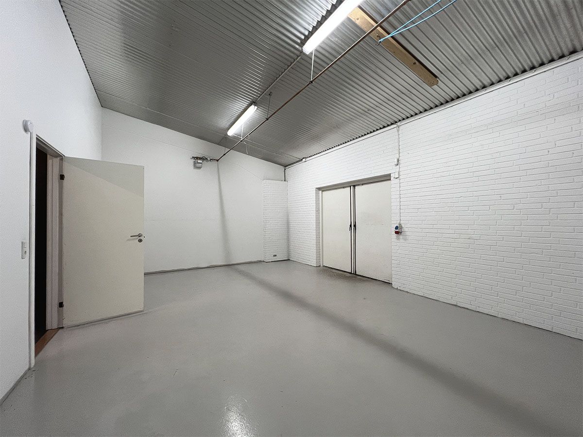 En stor og lys erhvervslejemål med hvide vægge, gulv og loft samt to hvide døre og en rørledning på loftet