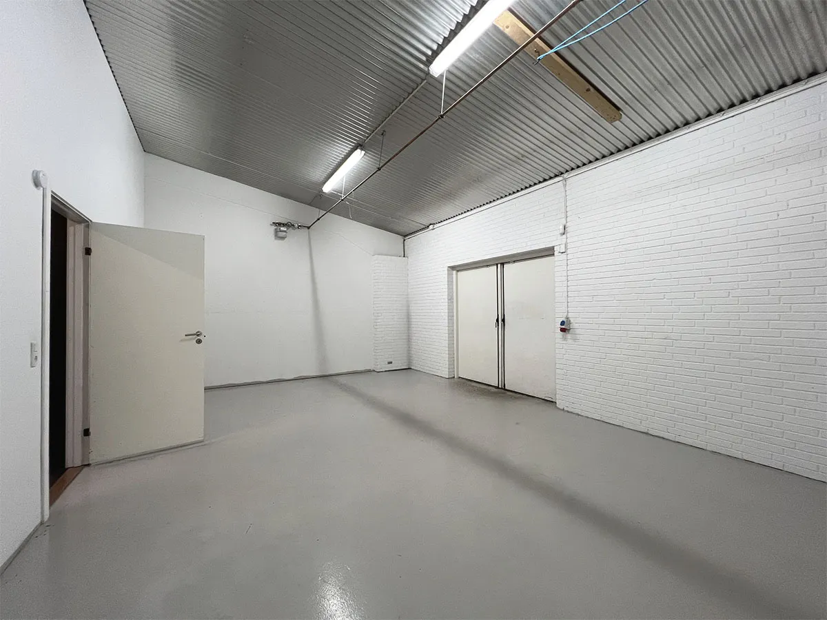 En stor og lys erhvervslejemål med hvide vægge, gulv og loft samt to hvide døre og en rørledning på loftet