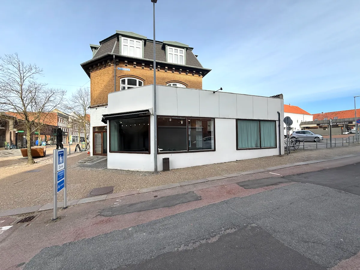 Et erhvervslejemål med hvid facade og røde vinduerne, hvor et schild med texten zone 25 er placeret til venstre