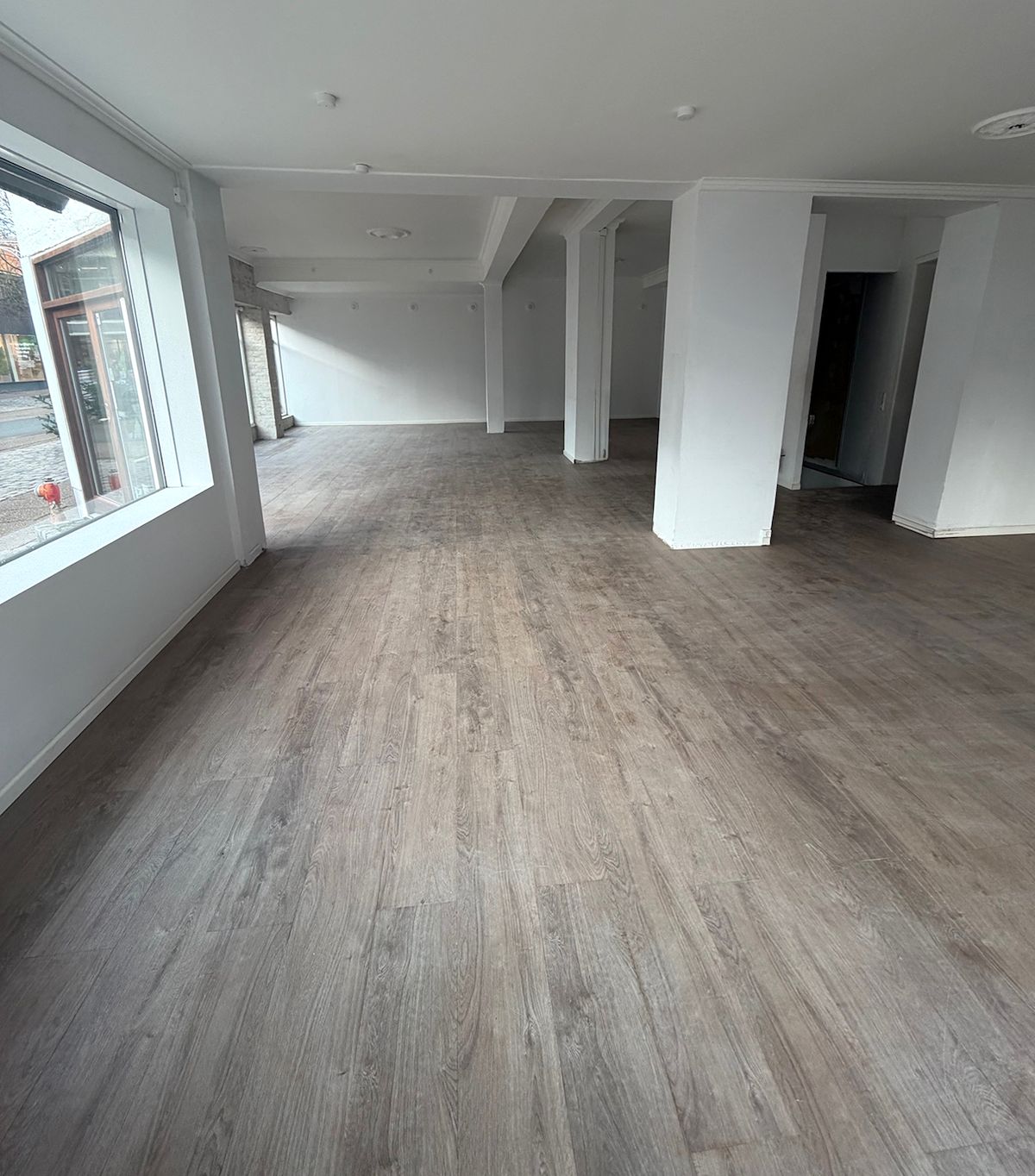Ledig erhvervslejemål i Hjørring med lyse gulvbelægning og lyse vægge. I stueplan er der store vinduer med udsigt til gågaden.