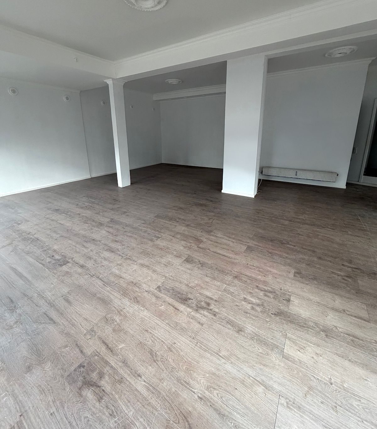 Store rum med lyse, lysegrå trægulve og hvide vægge. Værelserne har hvide søjler, og der er hvide lofter med indbygget belysning. Der er et radiator og et kabinet mod højre væg.