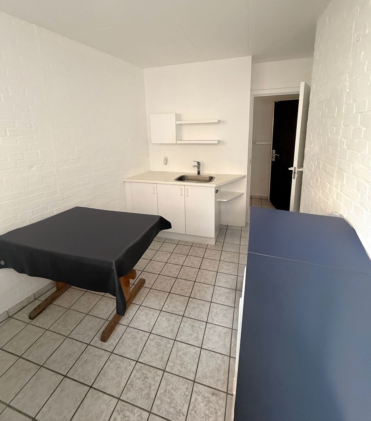 Et stort hvidt lokale med to smukke borddækninger i sort og blåt og et højt hjørne med hvide hylder og et rent køkken med en skarpt hvid skarp.