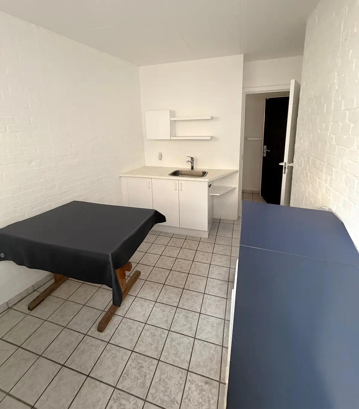 Et stort hvidt lokale med to smukke borddækninger i sort og blåt og et højt hjørne med hvide hylder og et rent køkken med en skarpt hvid skarp.