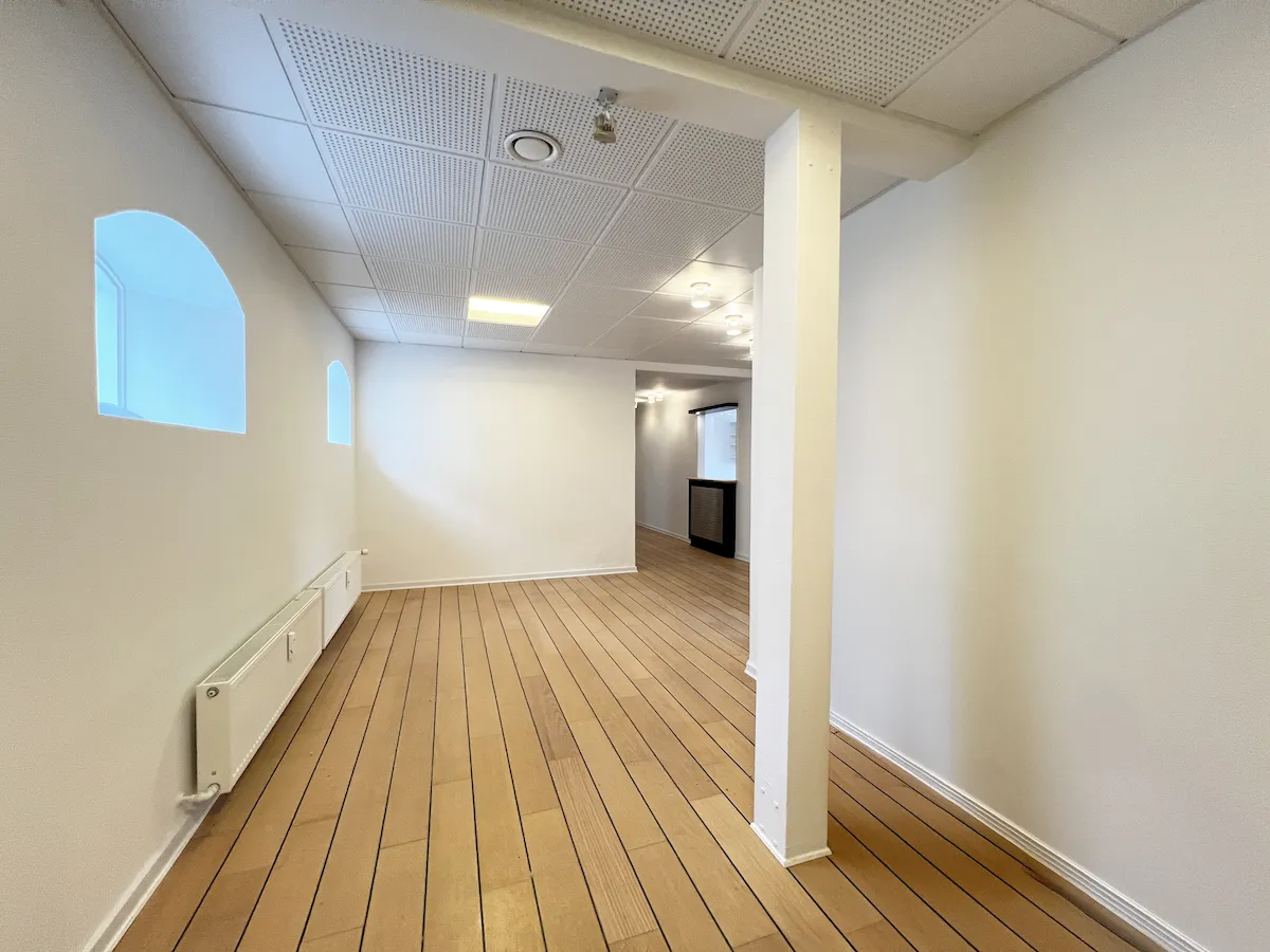 En rummelig lægeklink med en stor entre og venterum og 8 konsultationsrum. Hvide vægge og trægulve. Lyse blyagtige lofter med indlejrede lyspunkter