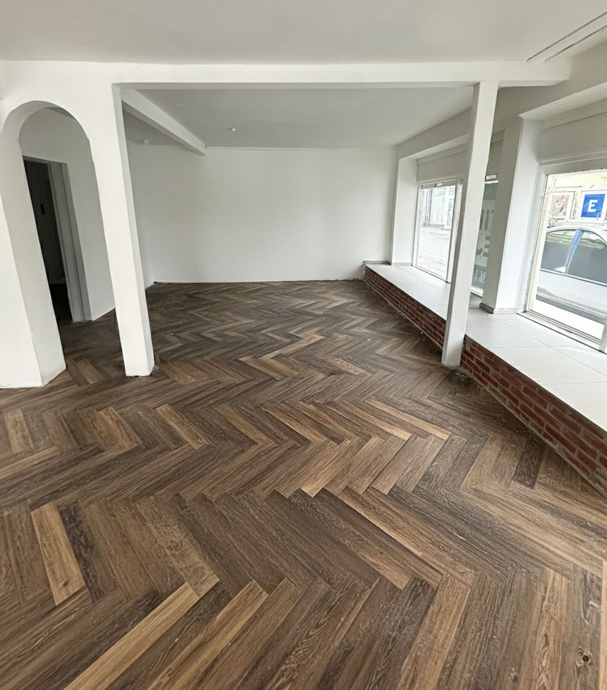 Butik med moderne trægulv og hvide vægge. De store vinduer lade lys strømme ind. Arkitektoniske detaljer som hjørnesøjler og bueformet dør.