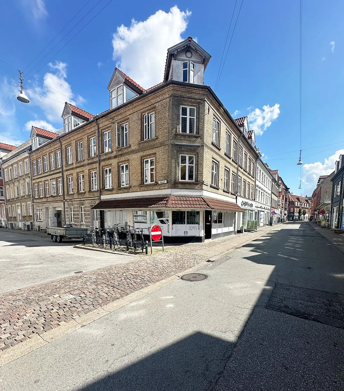 Lejlighed til leje i Aalborg, Reberbansgade 12A, 9000. Butik med mange vinduer og skrapelamper overfor. Mange cykler parkeret foran butikken