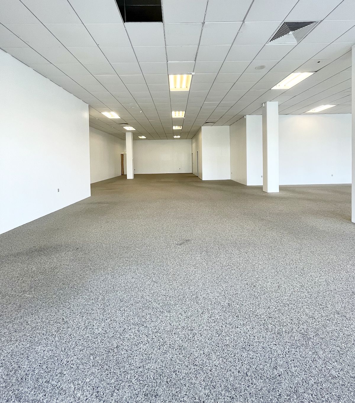 En stor og tom lejlighed med en lysgrå gulvbelægning, hvidt loft og vægge samt lyse gulvbelægning. Et hvidt gulv og hvide vægge.