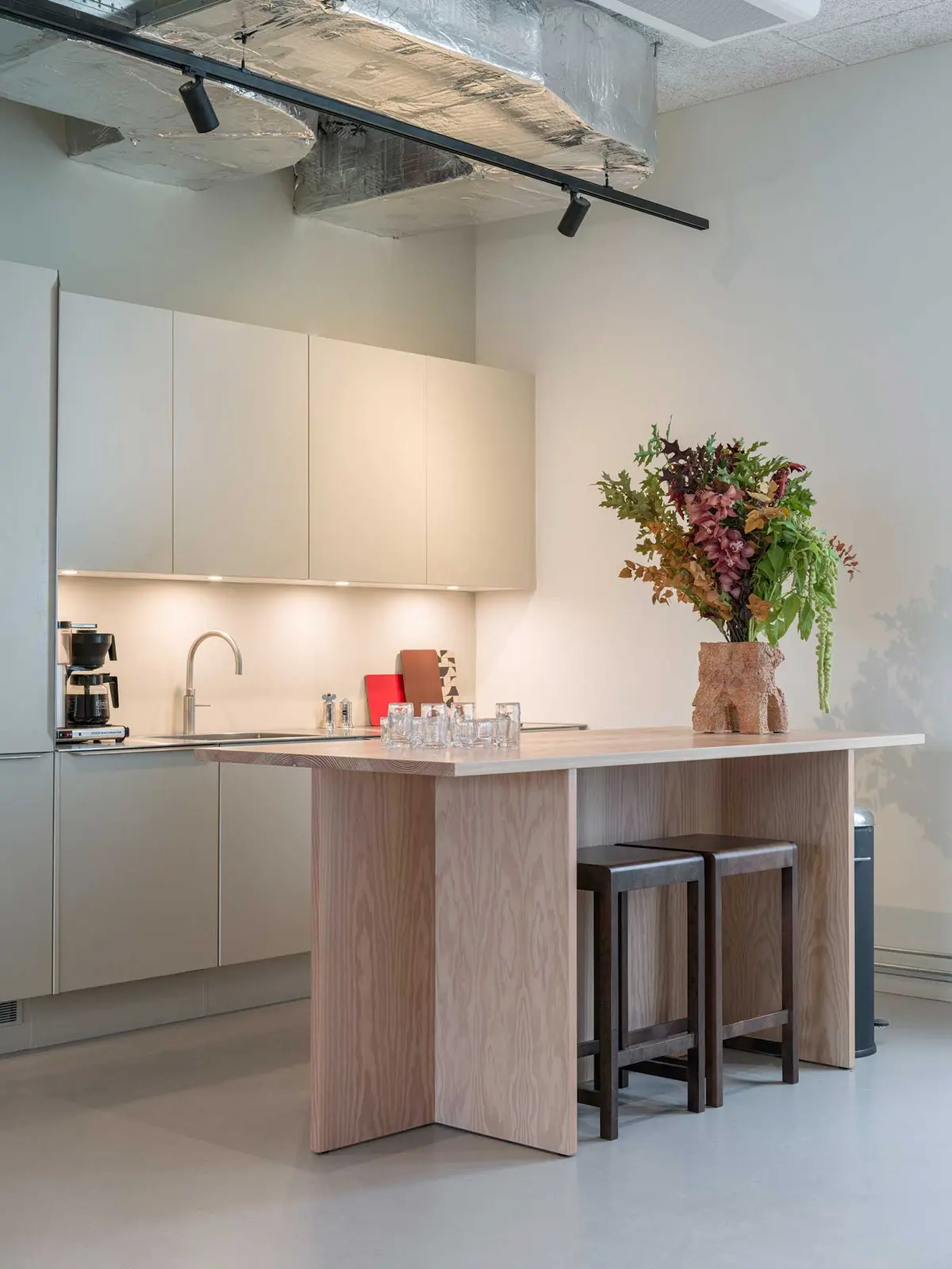 Moderne højloftet køkken med højt loft, hvidt køkken med møbler, glasflaske, blomster, træplade, kaffemaskine og håndvask med vandhane i hjertet af Carlsberg Byen