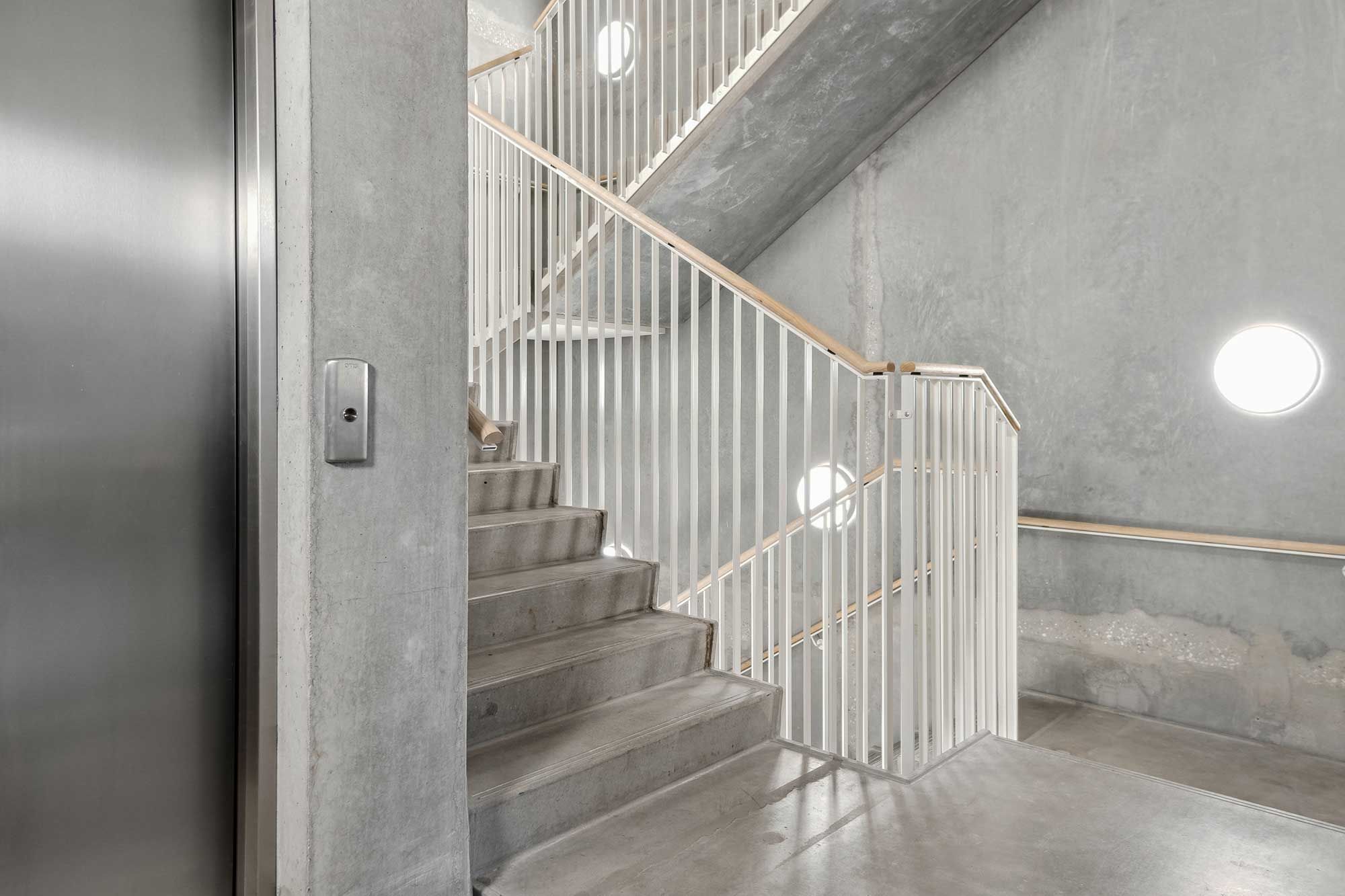 En højloftet og minimalistisk kontorlejemål med trappe og elevator i Carlsberg Byen med rå og lyse gulve, hvide stiger og højloftede rum