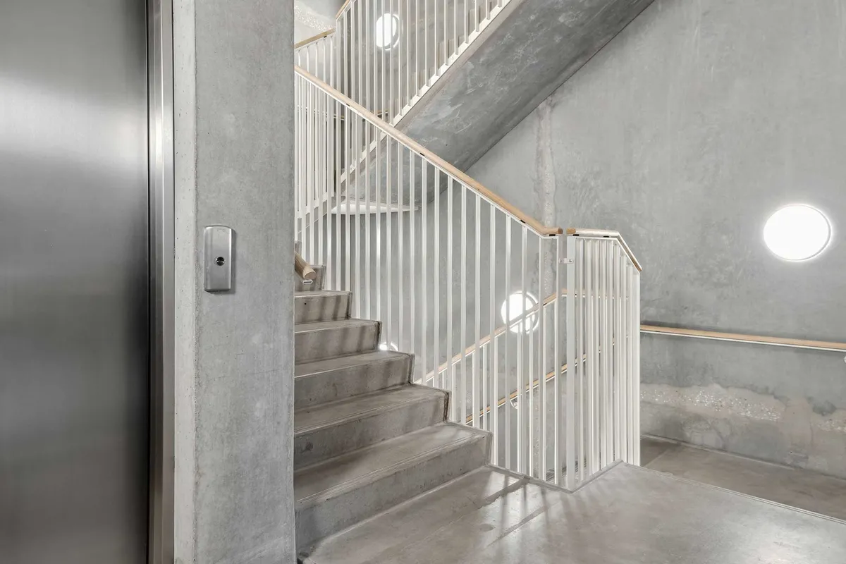 En højloftet og minimalistisk kontorlejemål med trappe og elevator i Carlsberg Byen med rå og lyse gulve, hvide stiger og højloftede rum