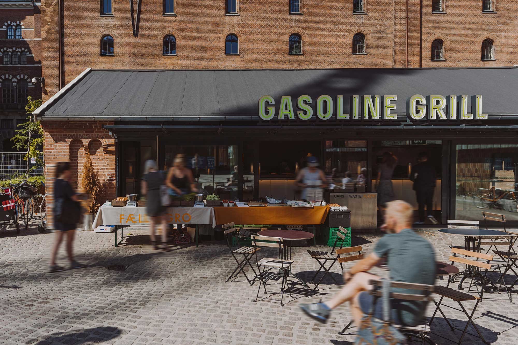 Man sidder og nyder mad på terrassen ved Gasoline Grill på Carlsberg Byen med små borde og stole rundt omkring