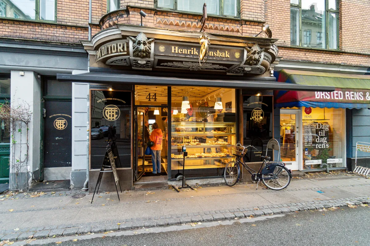 En café med navnet Henrik Ønsbak med nummer 44 og en cykel stående foran på gågaden og et kvinde i orange trøje stående i døren