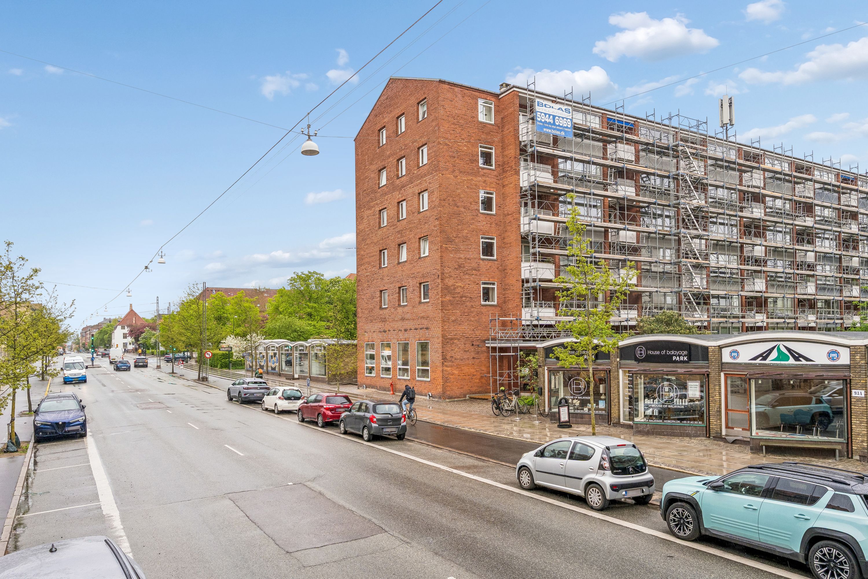Kontor til leje på Godthåbsvej 93A, 2000 Frederiksberg. Stående cykel og biler parkeret langs vejen. Bygning med opføring i gang, højt stigeværk og røde mursten