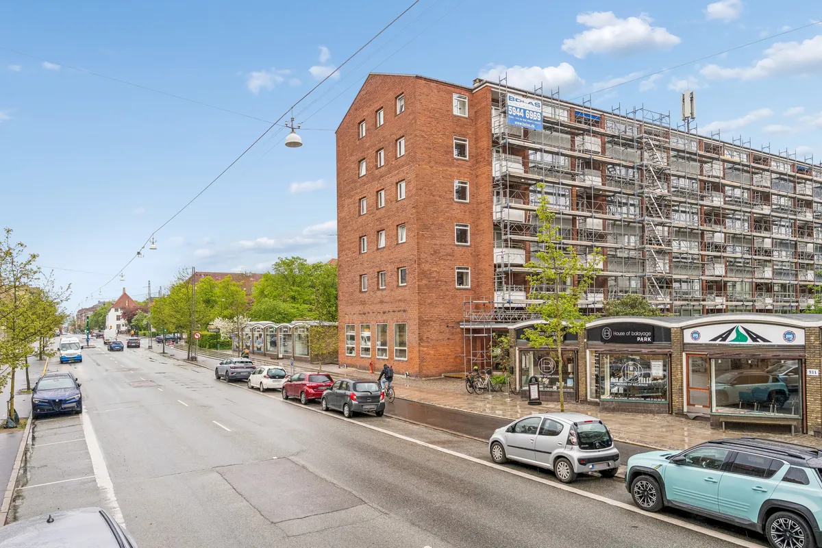 Kontor til leje på Godthåbsvej 93A, 2000 Frederiksberg. Stående cykel og biler parkeret langs vejen. Bygning med opføring i gang, højt stigeværk og røde mursten