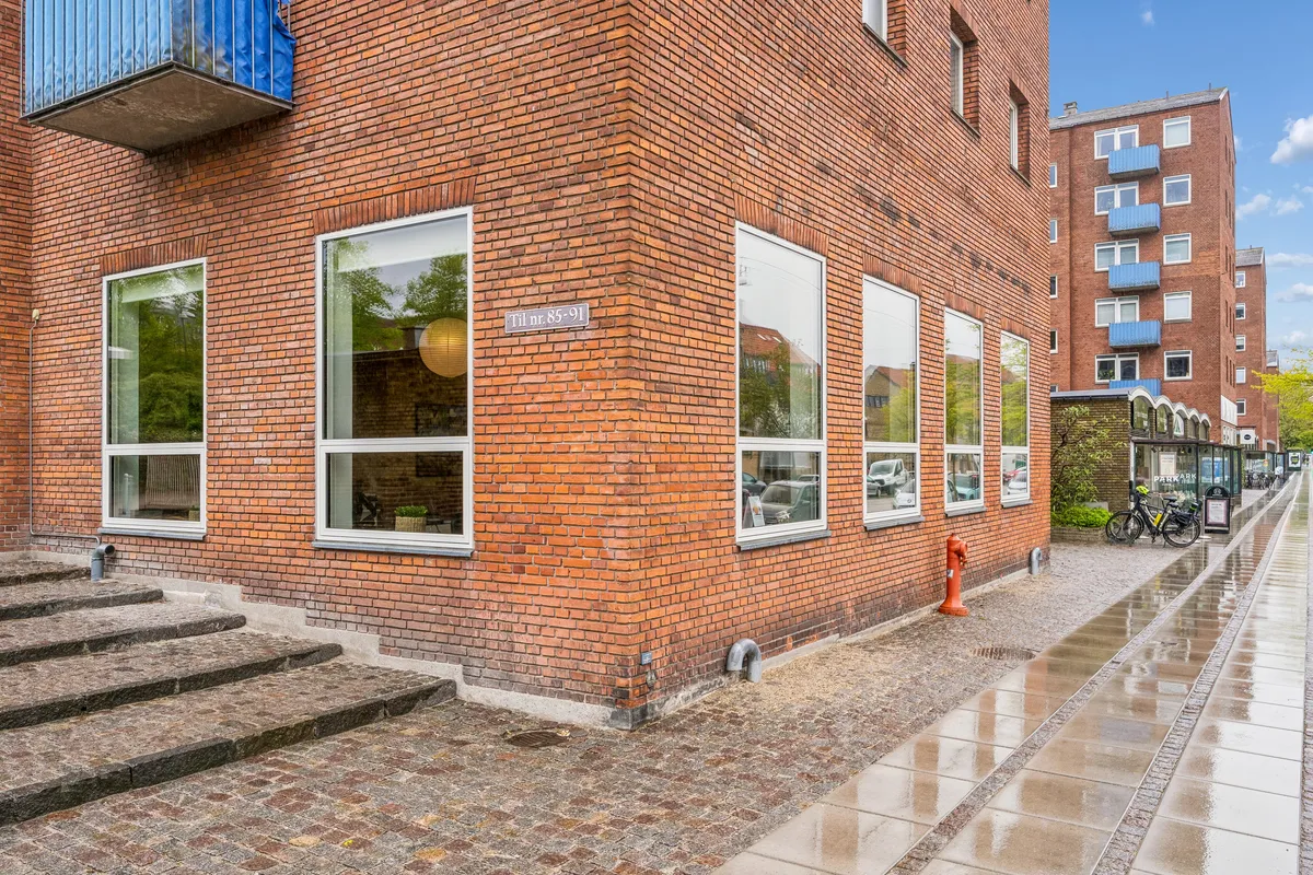 Kontorbyggeri med røde mursten og store glasvinduer på Godthåbsvej i Frederiksberg, med en vandpost og cykler parkeret til siden af gaden