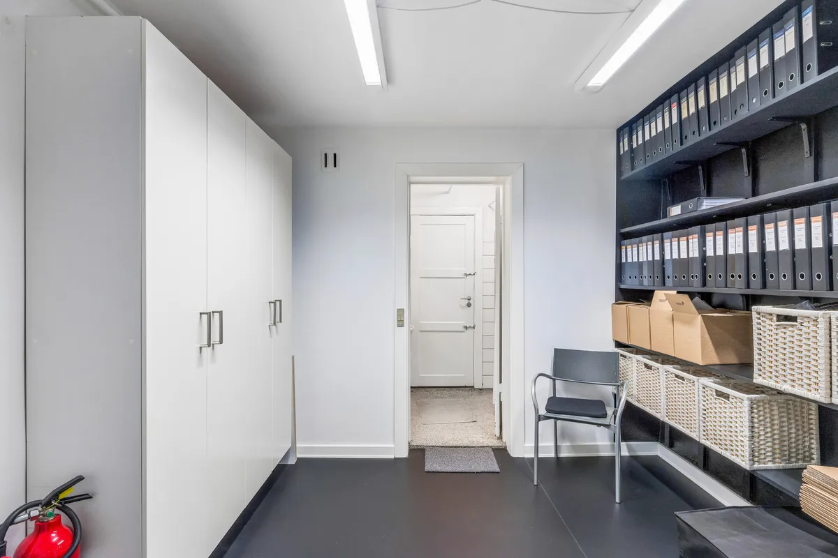Kontorlokaler med højloft, hvide vægge, møbler og en række opbevaringsbokse samt en stol og en brandværnsslange