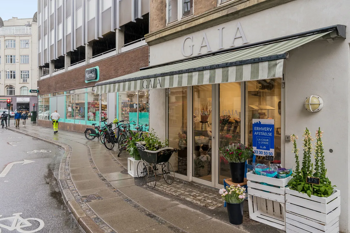 Butik til leje på Godthåbsvej 5, st. tv, 2000 Frederiksberg. Blomster og plantepots udenfor. Grønt og hvidt solskur med teksten "GAIA". Lys og vinduer.