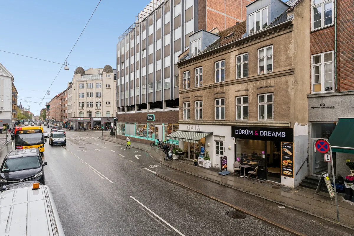 Gaden er fyldt med biler og busser med butikker og forretninger på begge sider, herunder caféer, yogastudier og en blomsterbutik