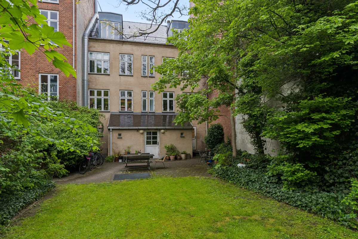 Smukke butikslejemål med indgang til baghaven, hvor der er en terrasse med blomster, lysekroner og grønne planter i solskin
