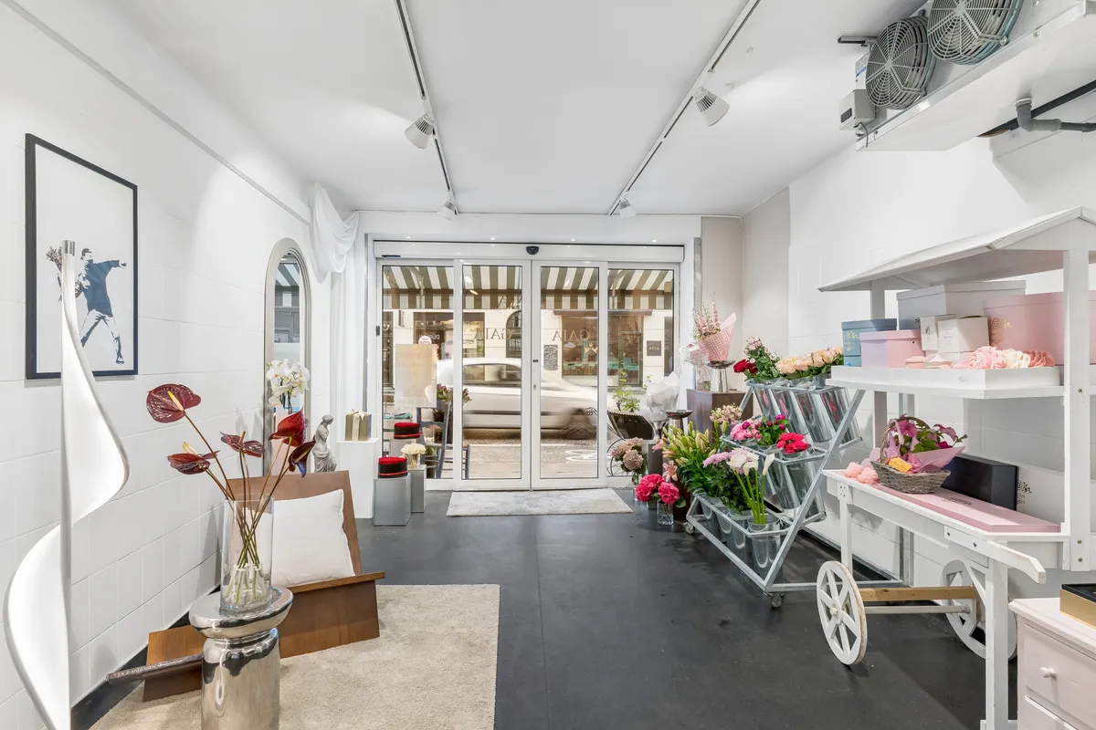 Indflytningsklar blomsterbutik med lyse møbler, lysekroner, blomster og røde og hvide kuffertstandere