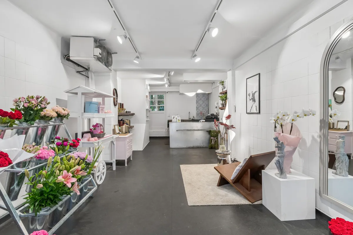 Flot og moderne butik med lyse gulve og hvide vægge. Vase med blomster og statuer på høje sokkelborde. Vasketøjsvogne med blomster. Ingen mennesker er synlige på billedet.