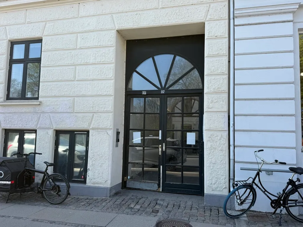 Kontor til leje på Nørre Farimagsgade 37, st., 1364 København K med parkerede cykler og et glasdør. Bygningen har hvide vægge med detaljer og nummeret 37.