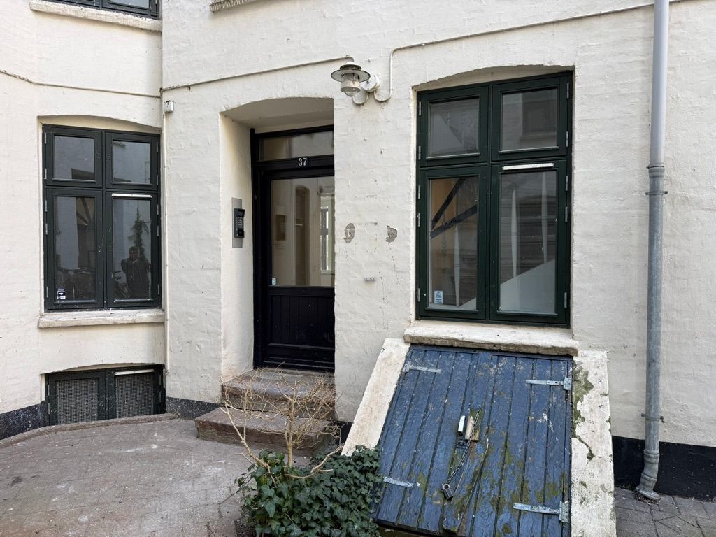 Kontor på Nørre Farimagsgade 37 med sort dør og træstiger, to grønne vinduerne med nummer 37 og lysekroner, gulv uden sne og grønne planter