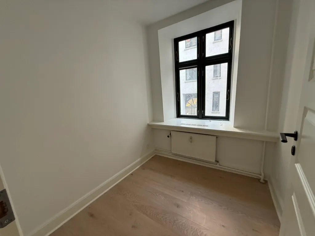 Lyst og rent kontor med trægulv, hvide vægge og vindue med udsigt til en bygning og gul vinduer
