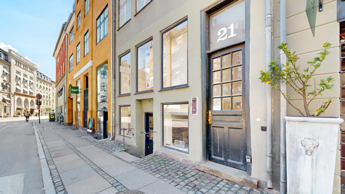 Et moderne og luksuriøst lejlighedshus med vinduer, døre og grønne planter langs gaden Gammel Mønt 21, st. i København