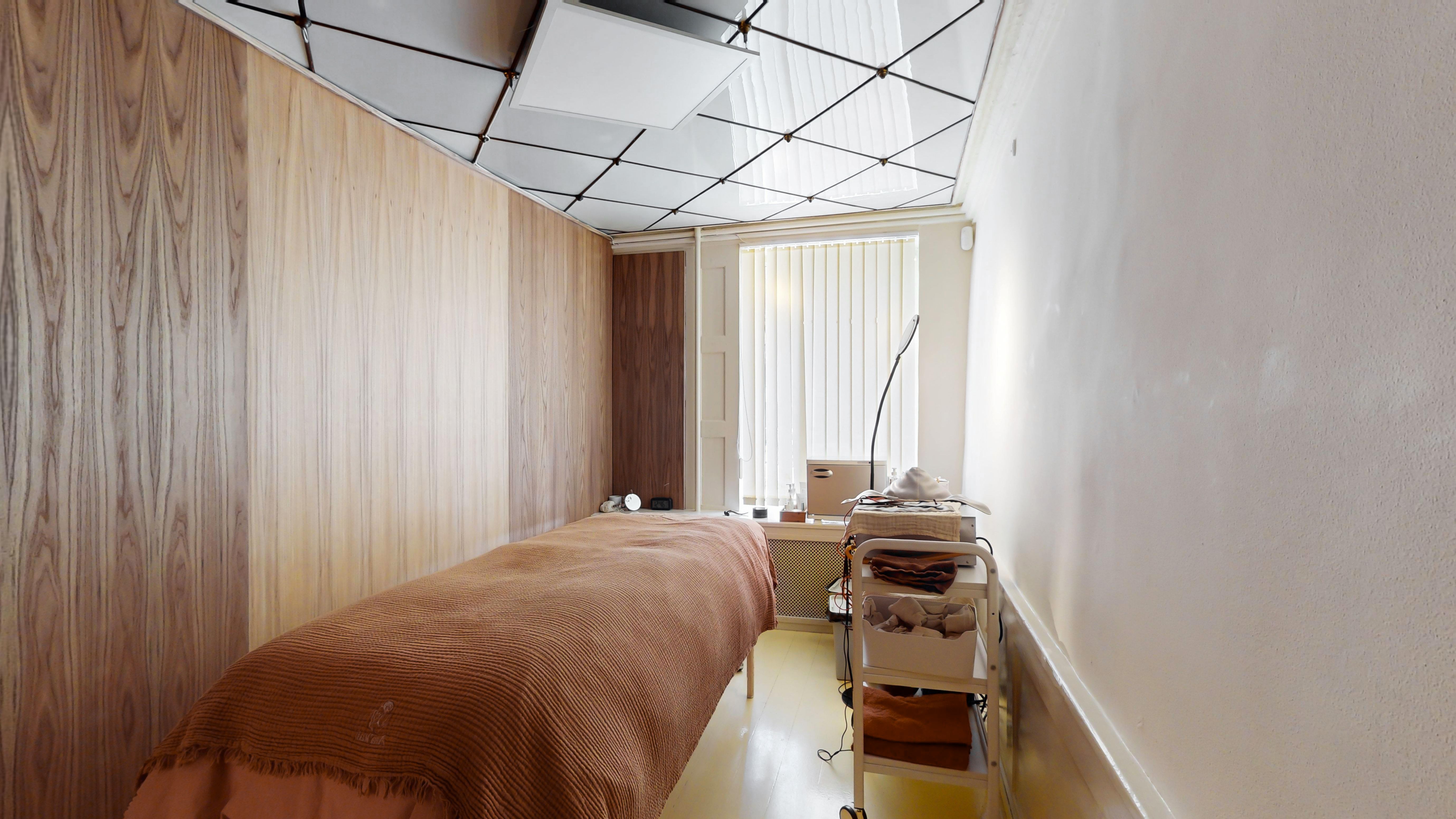 Et lille værelse med lysegul gulvbelægning og beige vægge med massagebord og en kasse med tæpper