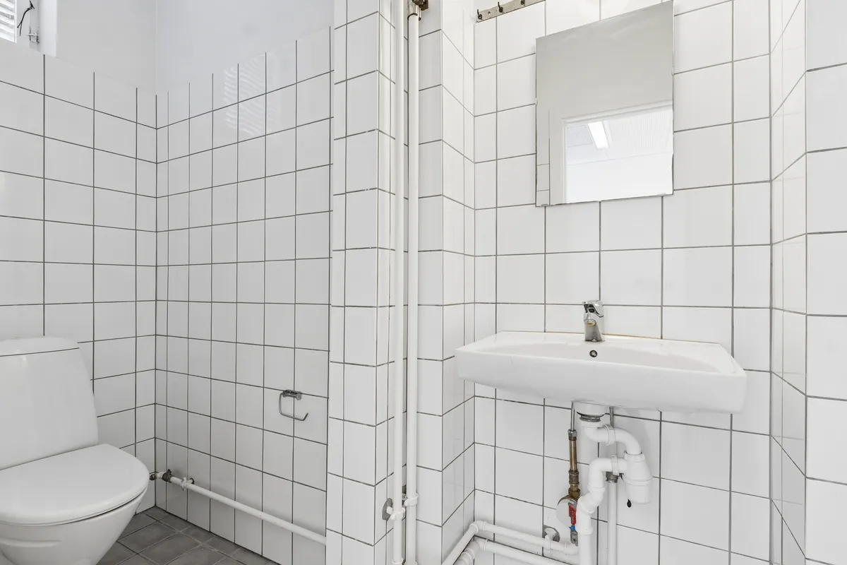 Lyst og rent toiletrum med hvide keramiske fliser og moderne design. Toiletstol og hvidt vasketøjsskab med håndklædeholder og spejl. Moderne renlighed og design i smukt og funktionelt toiletrum.